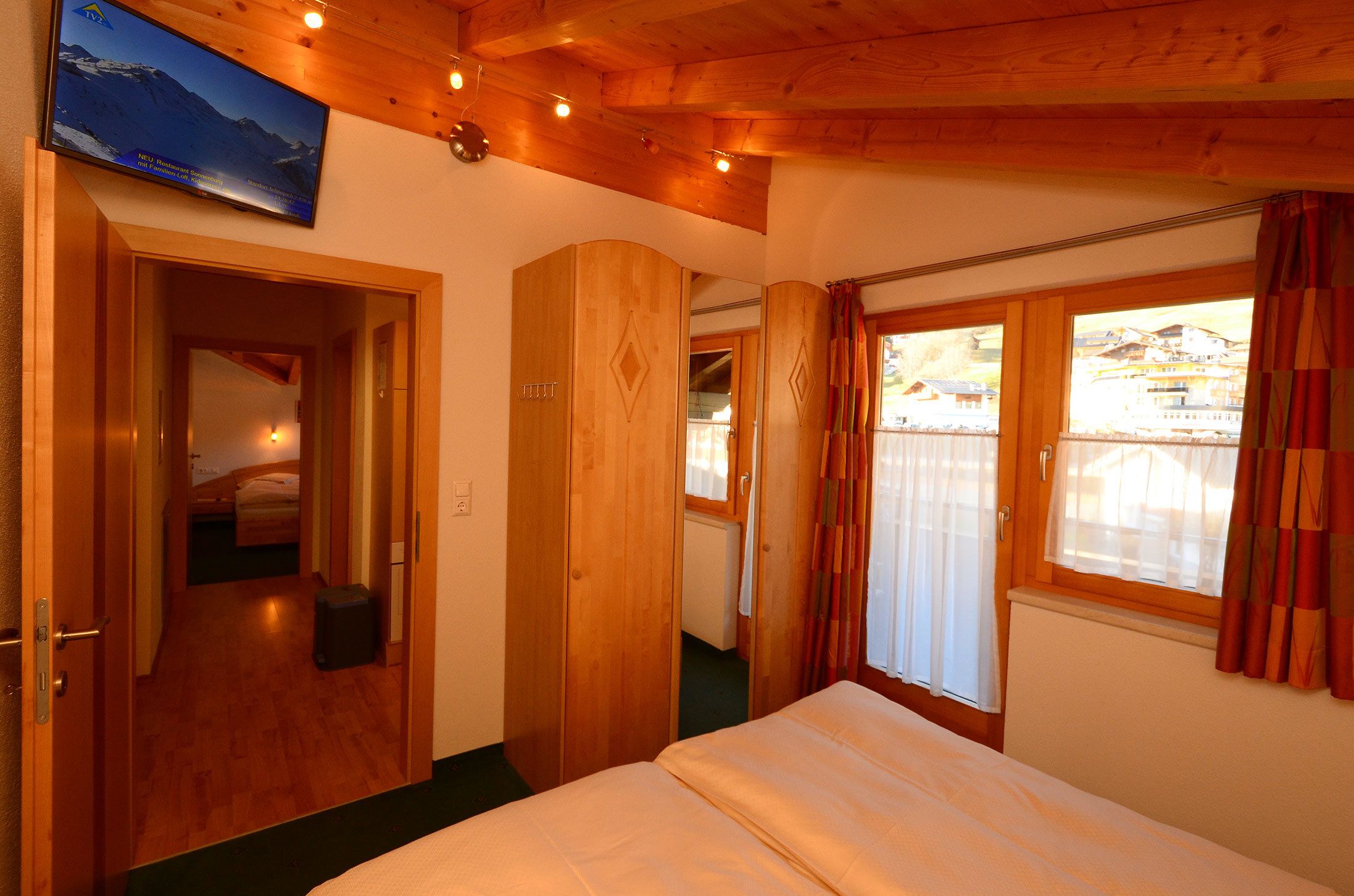 A hotel room with a bed, wooden walls, a television, and a window with curtains.