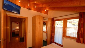 A hotel room with a bed, wooden walls, a television, and a window with curtains. - Edelweiss Ladis (Ladis)