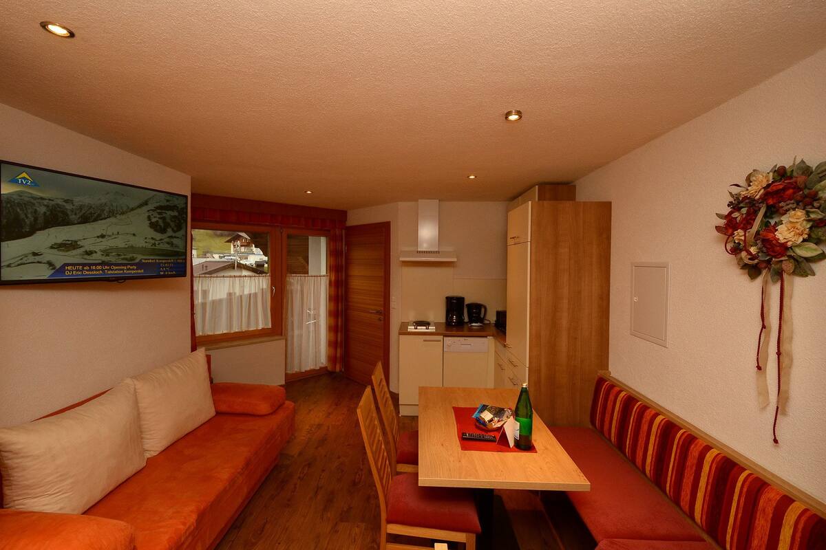 Una habitación compacta con sofá, una mesa de comedor con una botella, una pequeña zona de cocina y un adorno en la pared.