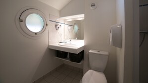 Ein kleines Badezimmer mit rundem Fenster, Toilette, Waschbecken und Spiegel.