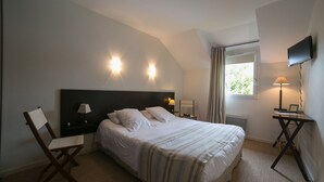 Ein Schlafzimmer mit einem großen Bett, zwei Nachttischen mit Lampen, einem Sessel, einem an der Wand montierten Fernseher und einem Fenster mit Vorhängen.