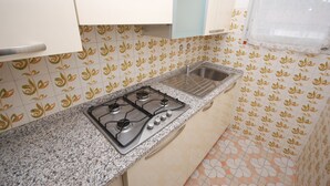 A kitchen with a gas stove, stainless steel sink, and patterned tiles. - Ville Canarino (Lignano Sabbiadoro)