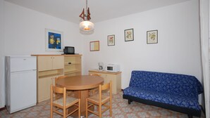 A small, compact living space with a kitchenette, a dining area with a table and chairs, a sofa, and a patterned floor. - Ville Canarino (Lignano Sabbiadoro)