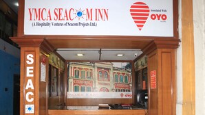 Un comptoir d’accueil avec une enseigne indiquant « YMCA Seac M Inn », ainsi qu’une horloge et un logo en forme de cœur.