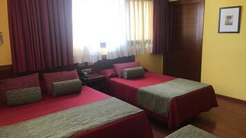 A hotel room with two beds, each with red bedding and green throw pillows. There is a wooden door on the right and a window with curtains.