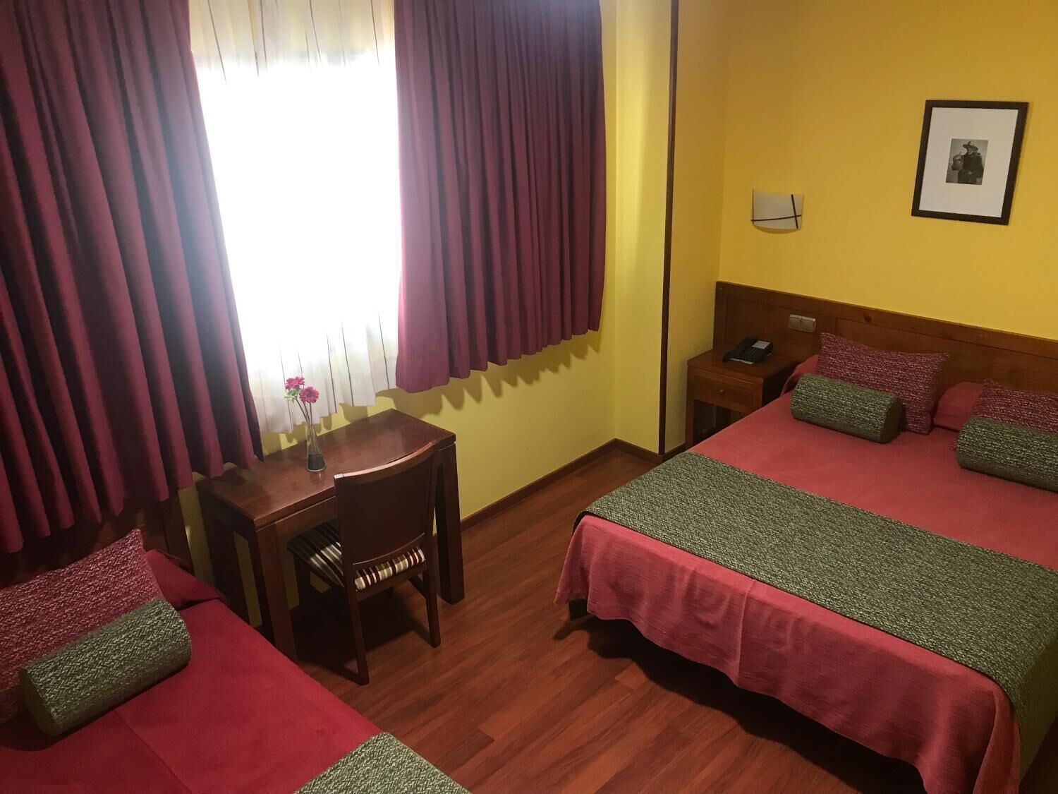 A hotel room with two beds, a wooden desk, a chair, a nightstand, and a bedside table.