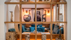 A cozy room with a wooden arched shelf displaying various decorative items, including animal carvings and a globe. Blue upholstered chairs and a small table with a candle are visible. - Bergnest - Frühstückspension Katschberg (Sankt Michael im Lungau)