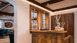A wooden reception desk with a window, a heart-shaped wall decoration, and a seating area with teal chairs. - Bergnest - Frühstückspension Katschberg (Sankt Michael im Lungau)