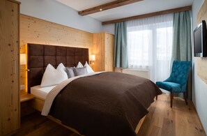 A bedroom with a large bed, wooden headboard, a blue armchair, and a TV mounted on the wall. - Bergnest - Frühstückspension Katschberg (Sankt Michael im Lungau)