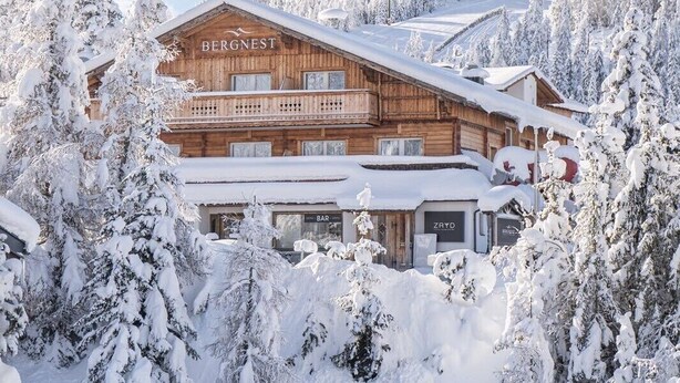 A wooden chalet named BERGNEST with a bar and restaurant named ZRYD, surrounded by snow-covered trees and a ski slope in the background. - Bergnest - Frühstückspension Katschberg (Sankt Michael im Lungau)