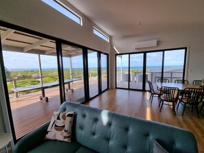 Une pièce spacieuse dotée d’une grande porte-fenêtre coulissante donnant sur une terrasse extérieure avec vue sur l’océan.