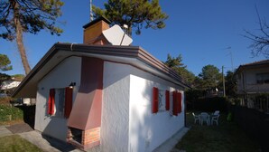 A small, single-story house with a sloped roof and red shutters. - Ville La Tana - Paola (Lignano Sabbiadoro)
