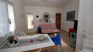 A living room with a dining table, chairs, a sofa, and a TV. - Ville La Tana - Paola (Lignano Sabbiadoro)