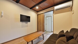 A living room with a wooden bench, a brown sofa, a flat-screen TV, and an air conditioning unit. - Shiki Tofukuji (Kyoto)