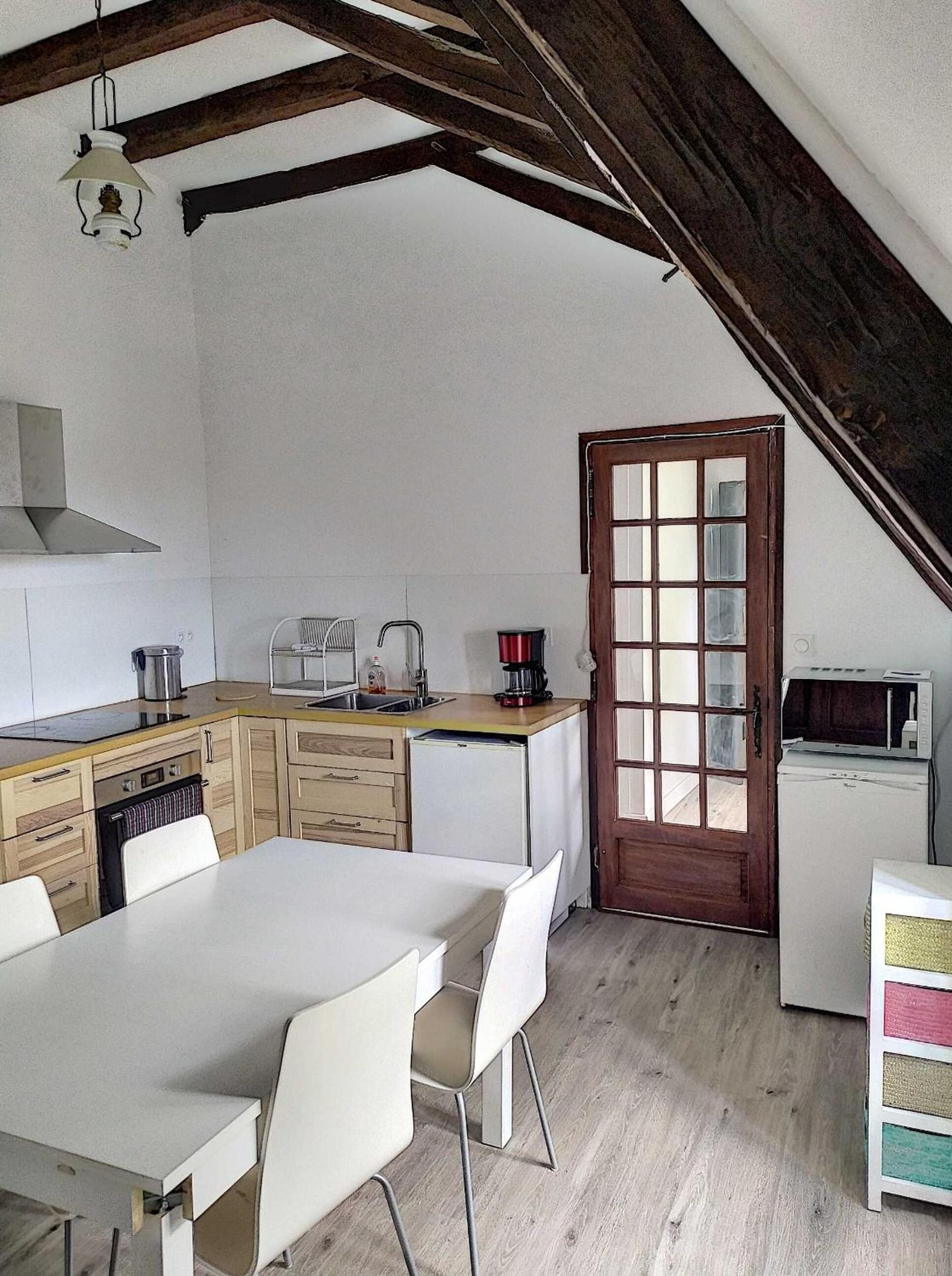Una cocina compacta con vigas de madera, una mesa blanca y sillas.
