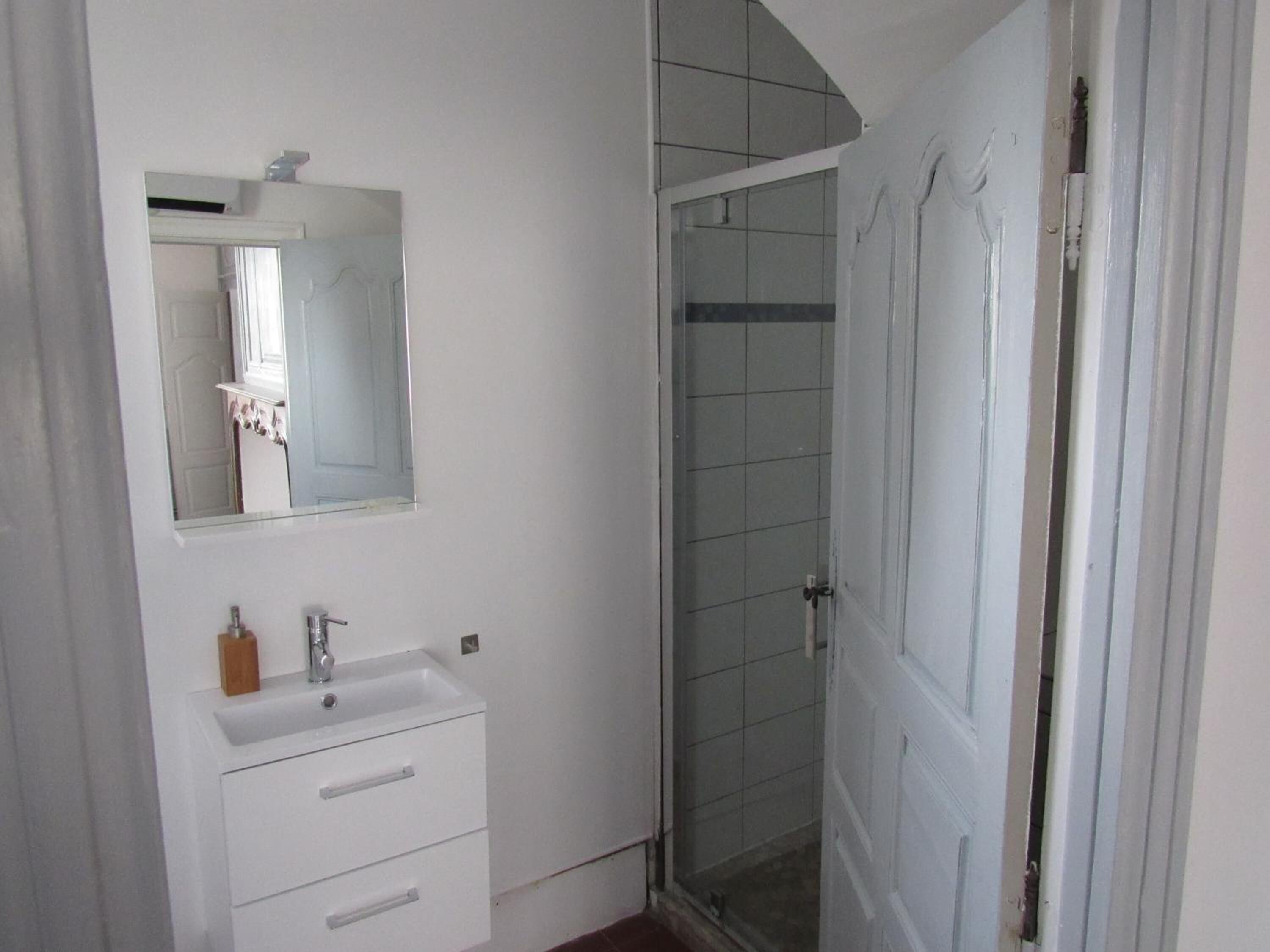 Un baño con lavabo blanco, espejo y mampara de ducha.