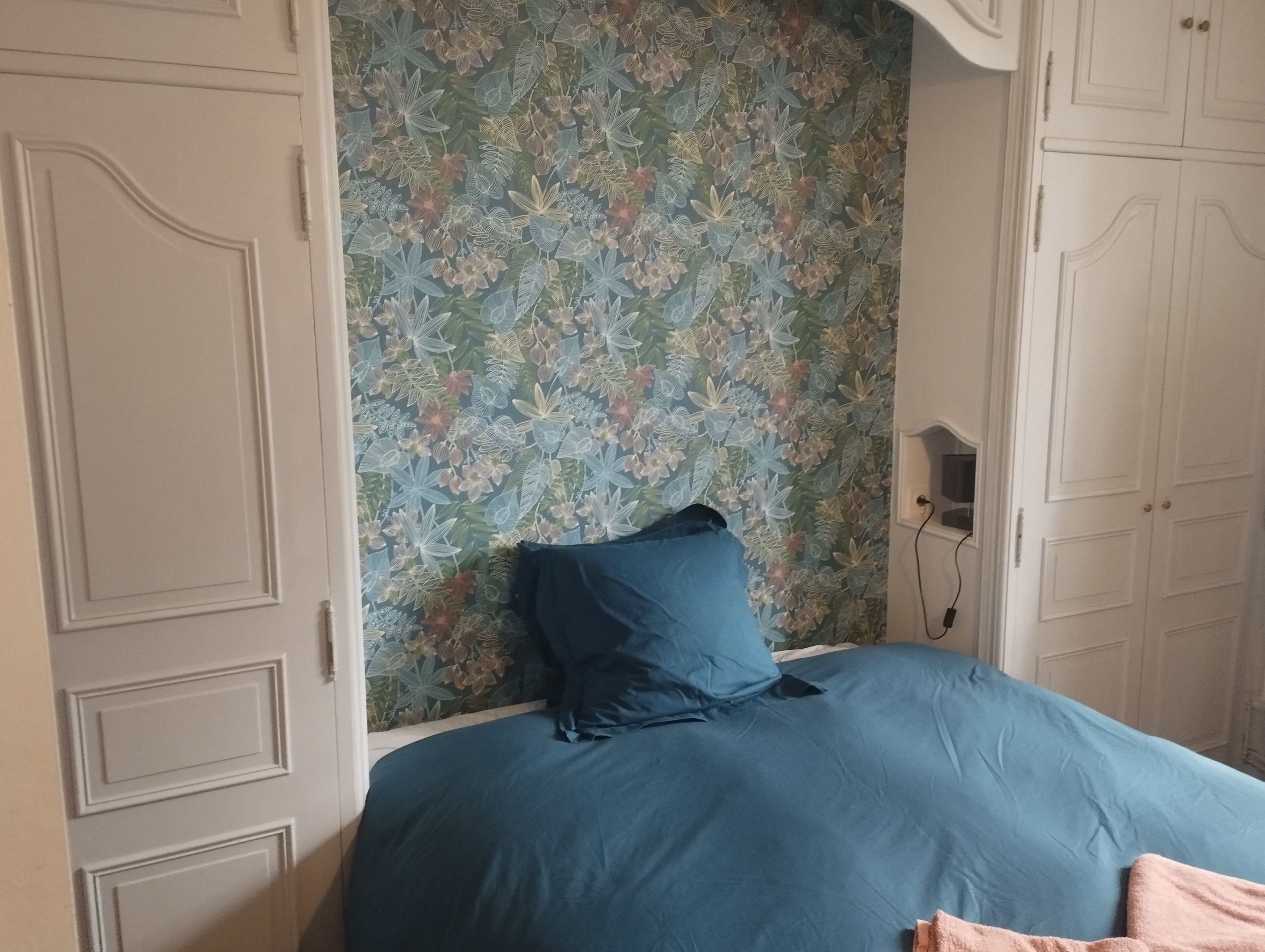 Una camera da letto con carta da parati floreale, copriletto blu e ante di armadio bianche.