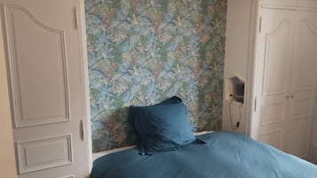 Una camera da letto con carta da parati floreale, copriletto blu e ante di armadio bianche.