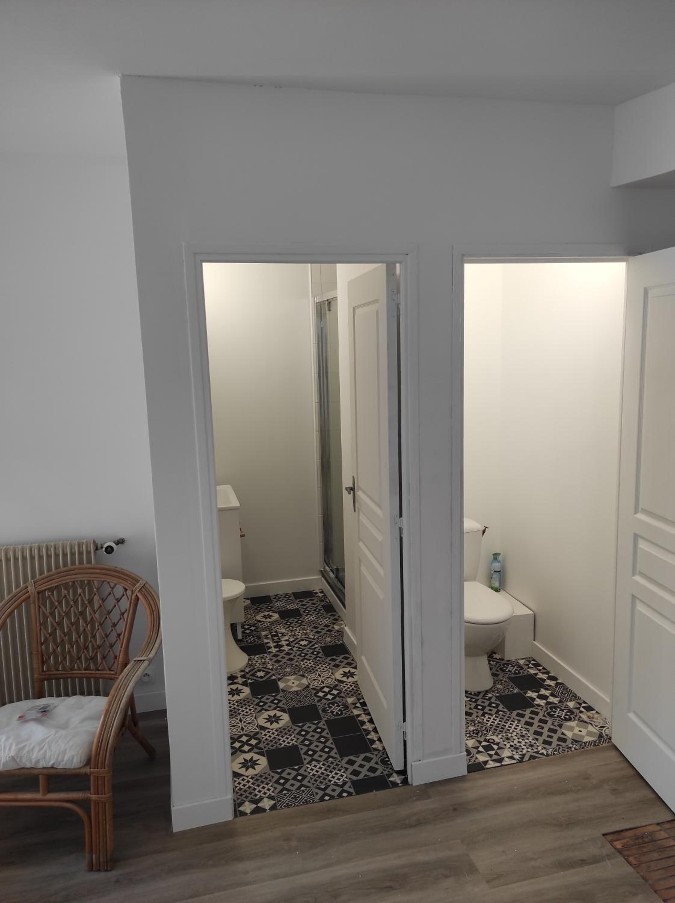 A hallway leading to a bathroom with patterned floor tiles, a white toilet, and a wicker chair.