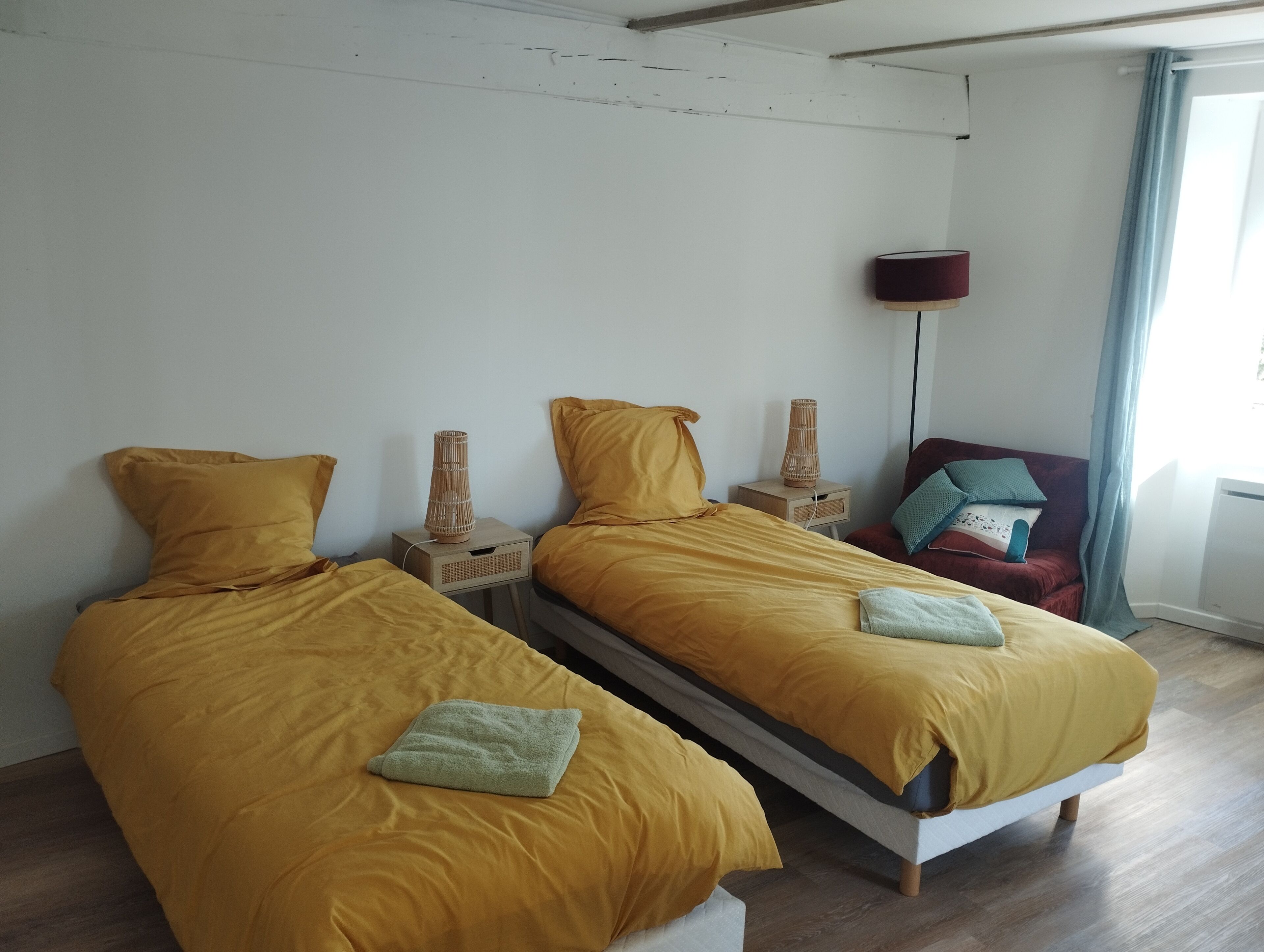 A room with two beds, a nightstand, a lamp, and a chair.