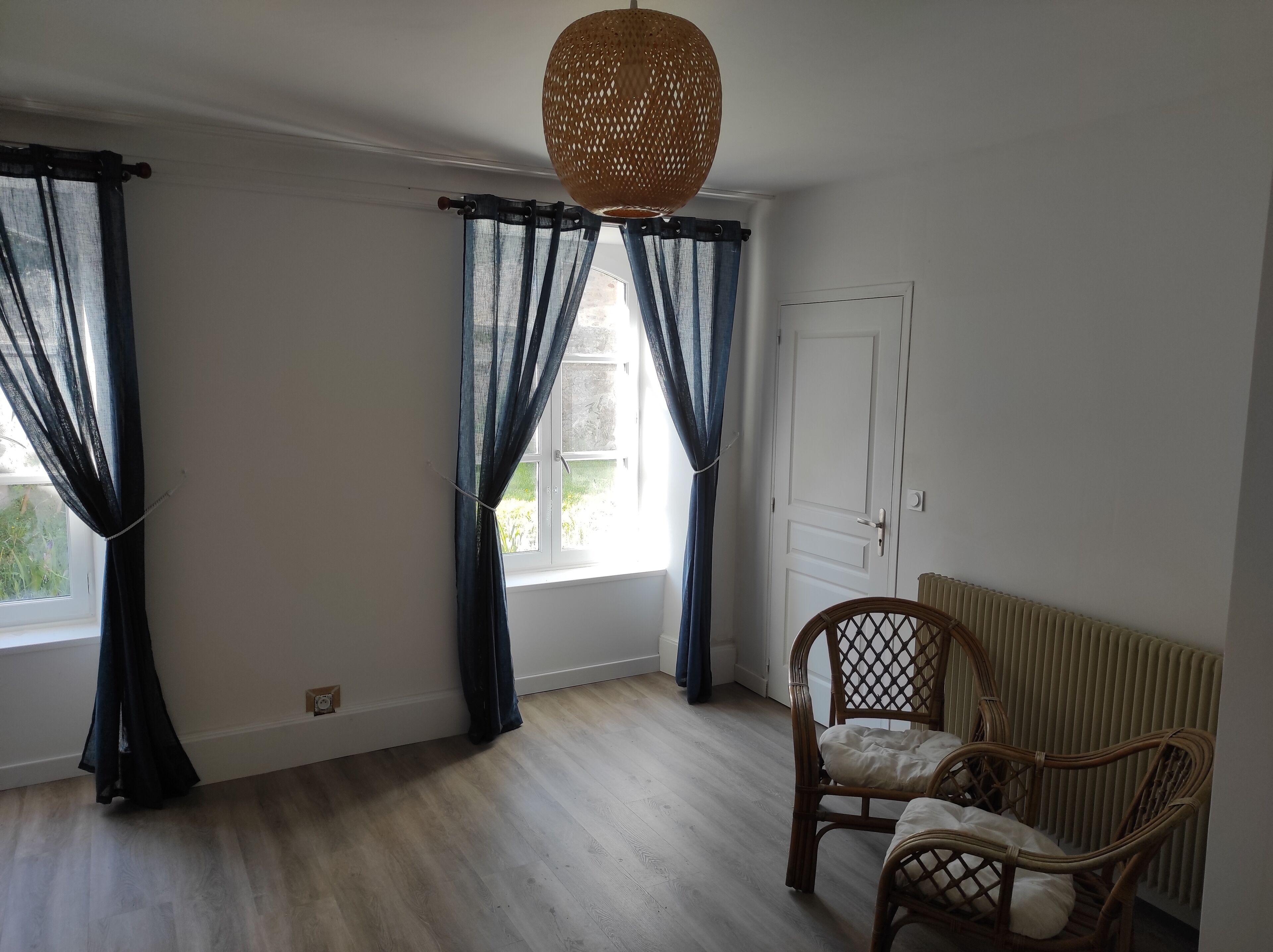 A room with a large window, a wicker chair, and a radiator.