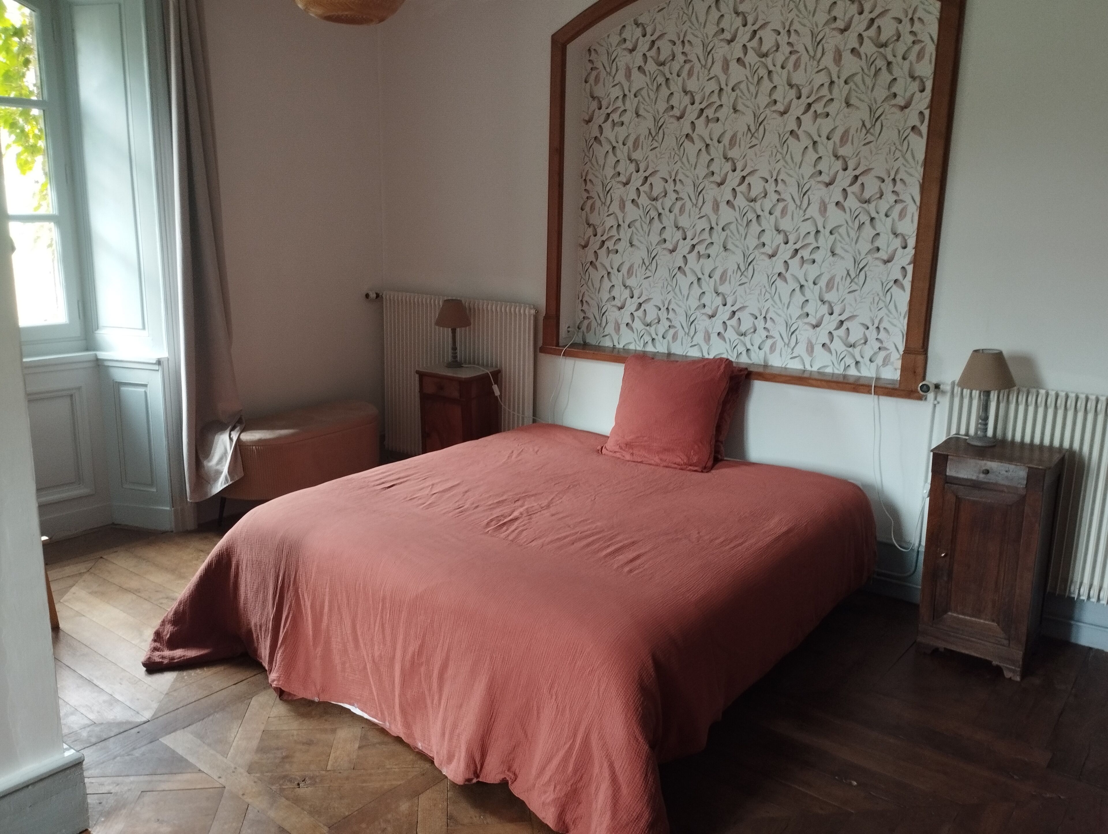Une chambre à coucher avec un grand lit, une table de chevet, une lampe, un radiateur et une fenêtre avec des rideaux.