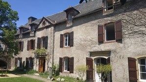 A two-story stone building with multiple windows and doors, surrounded by a well-maintained lawn. - L' Arche d' Yvann (Campuac)