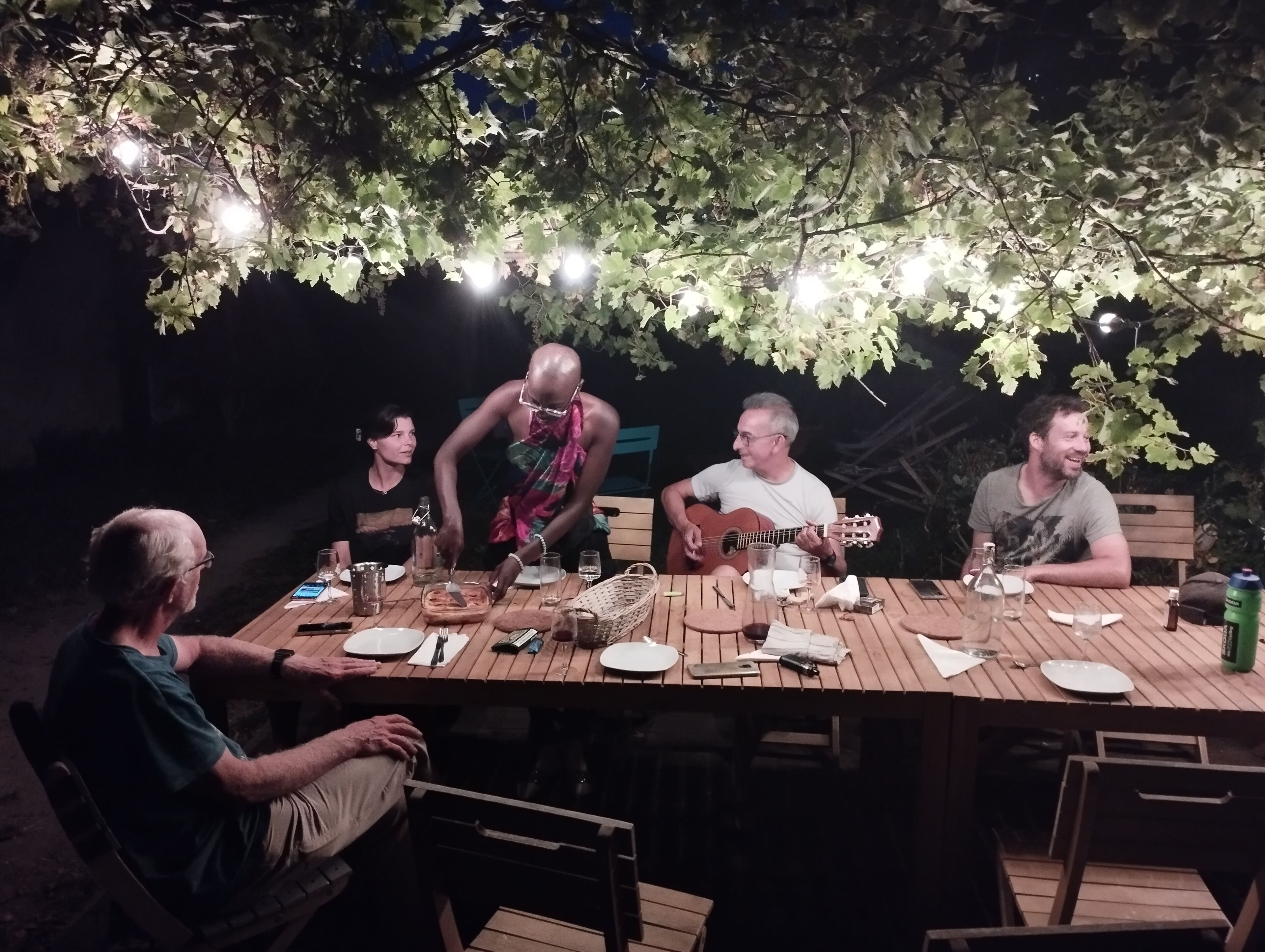 Un grupo de personas cenando al aire libre por la noche, con luces colgantes.