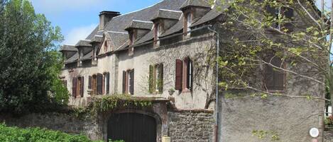 A historic stone building with a large central entrance and multiple windows with shutters.