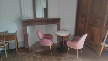 A room with a wooden floor, a fireplace, two pink chairs, a small round table, and a wooden cabinet.