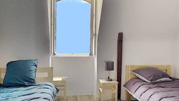 A small, simple room with two beds, a desk, and a window.