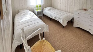Een kamer met twee bedden, een stoel, een dressoir, een nachtkastje en een raam met jaloezieën.