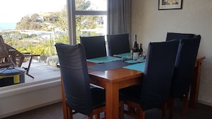 A dining area with a wooden table, four chairs, a red pendant light, and a view of the outdoors through large windows.