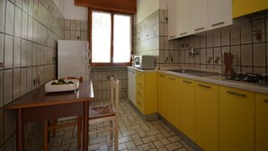 A compact kitchen with yellow cabinets, a white refrigerator, a microwave, and a sink. - Ville Missana (Lignano Sabbiadoro)