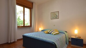 A bedroom with a bed, two bedside tables, a window, and a wall-mounted picture. - Ville Missana (Lignano Sabbiadoro)