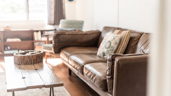 A cozy living room with a brown leather sofa, a wooden coffee table, and a patterned throw pillow.