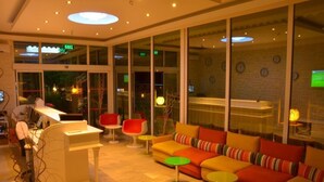 A modern lobby with a reception desk, seating area with colorful sofas and chairs, large windows, and a visible bar area. - Life Elite Hotel (Manavgat)