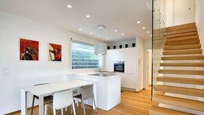 A modern kitchen with a central island, white cabinetry, and a wooden staircase. - Ville Summer (Lignano Sabbiadoro)