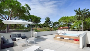 A rooftop terrace with a modern outdoor seating area, including a sofa, chairs, and a table. There is a hot tub and a pergola providing shade. - Ville Summer (Lignano Sabbiadoro)