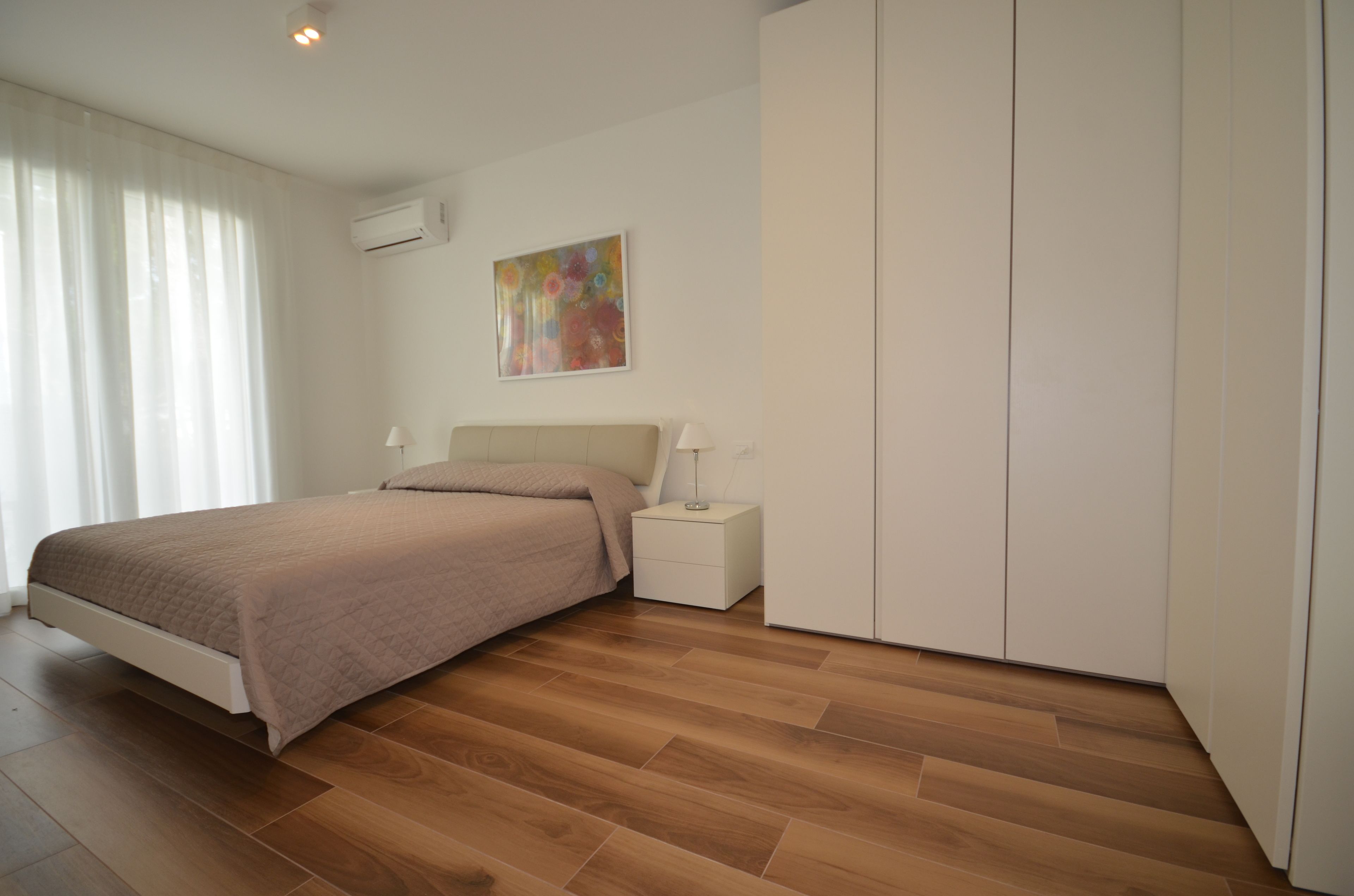 A bedroom with a bed, nightstands, a wardrobe, and a painting on the wall.