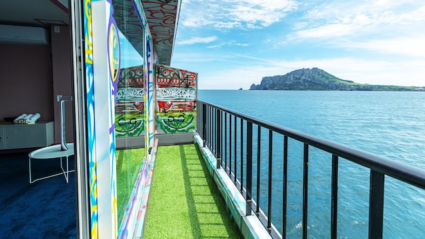 A balcony with a view of the sea and a mountain, featuring colorful graffiti on the railings. - Island.F Jeju (Seogwipo)