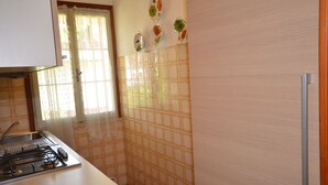 A kitchen with a gas stove, a sink, and a window with curtains. - Villedda (Lignano Sabbiadoro)