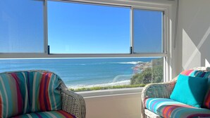 A room with a view of the ocean through a large window, wicker chairs with striped cushions, and a white wall. - Avalon 2- One of the best views that Yamba has to offer. (Yamba)