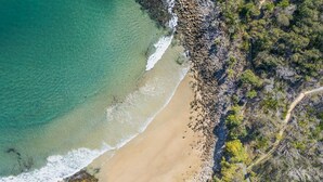 An aerial view of a beach with clear turquoise water, a sandy shore, and a rocky outcrop with sparse vegetation. - Avalon 2- One of the best views that Yamba has to offer. (Yamba)