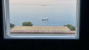 Vista desde una ventana que muestra una terraza de madera con vista a una masa de agua tranquila y un bote pequeño.