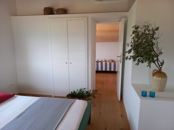 A bedroom with a bed, a wardrobe, a plant, and a small table with hats.