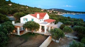 Una casa blanca con techo rojo, rodeada de árboles y vista al mar.