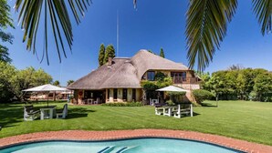 Een huis met een groot zwembad, omringd door een verzorgd gazon en palmbomen.