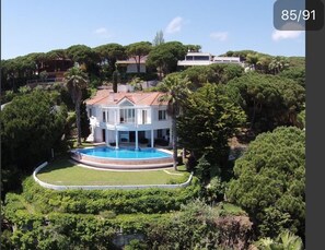 A large, white, two-story house with a circular pool surrounded by a low wall and lush greenery. - Villa Tortuga12, Spain, Lloret de Mar (Lloret de Mar)
