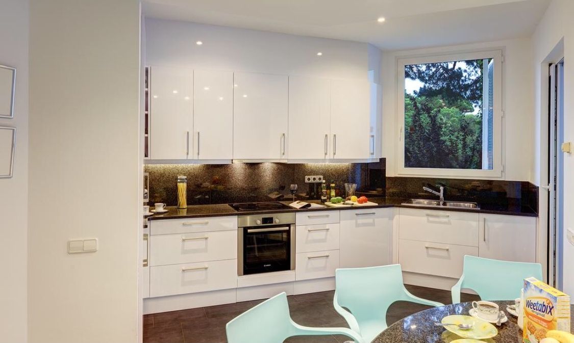 A modern kitchen with white cabinets, a black countertop, and a window providing a view of greenery outside.